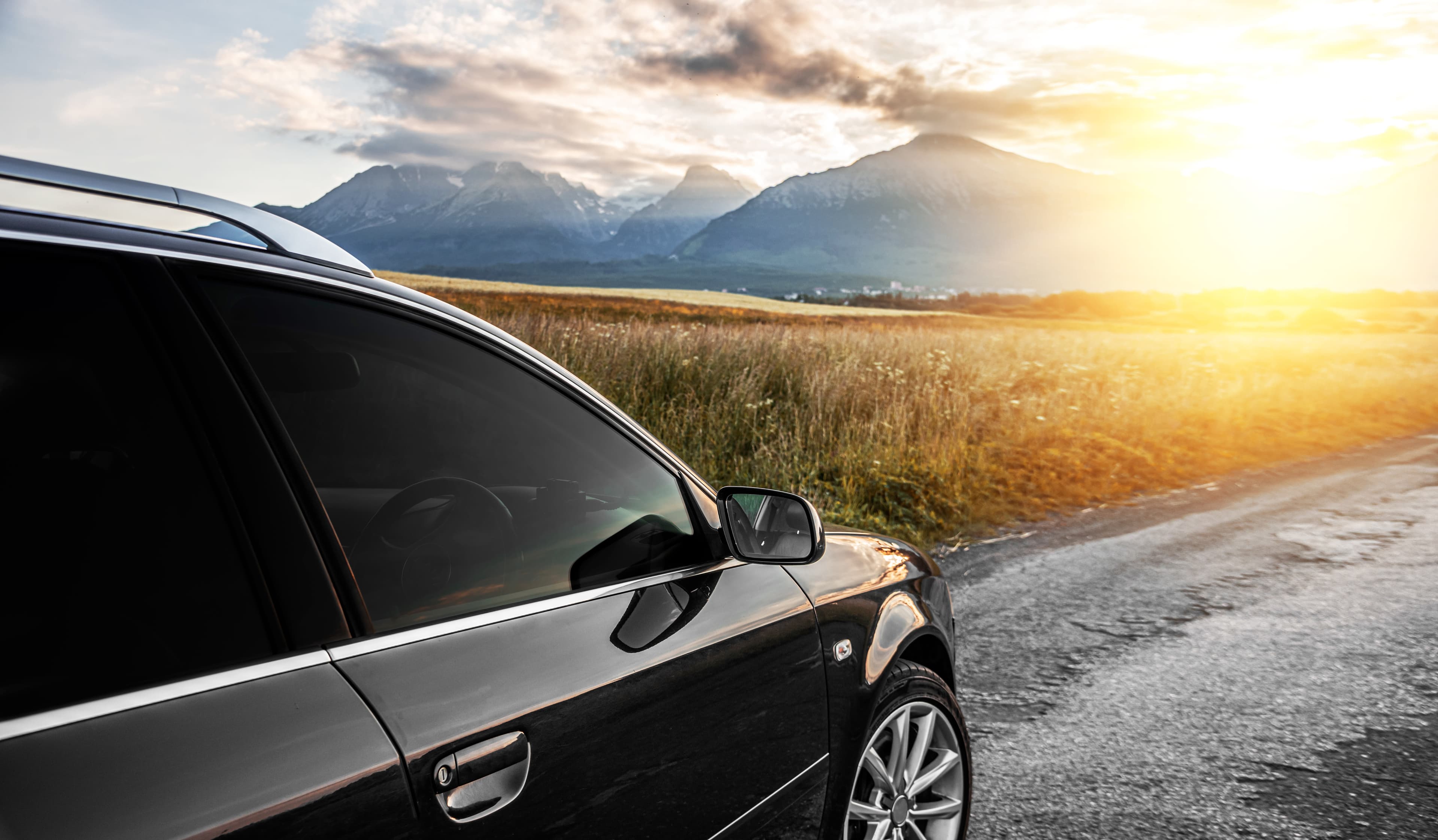 SUV driving on a road towards mountains at sunset